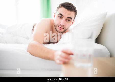 L'Uomo svegliati la mattina nel suo letto e si estendono al vetro con l'acqua. Foto Stock