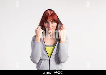 Attraente giovane donna fitness in grigio con cappuccio Felpa. Studio shot su sfondo grigio. Foto Stock