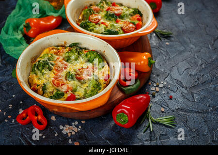 Frittata con i broccoli, spinaci, peperoni e pomodori in due forme ceramiche per la cottura. Italian frittata con verdure. Foto Stock