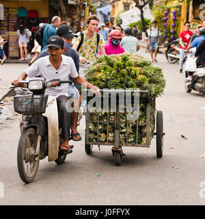Vista su piazza del popolo in sella a una moto e tira un carrello pieno di ananassi dietro di loro a Hoi An, Vietnam. Foto Stock
