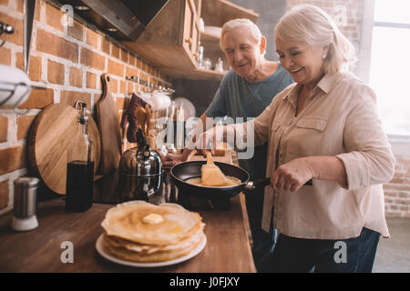 Coppia senior cucinare frittelle su cucina a casa Foto Stock