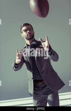 Bello elegante uomo in occhiali cerca di catturare un pallone da rugby Foto Stock