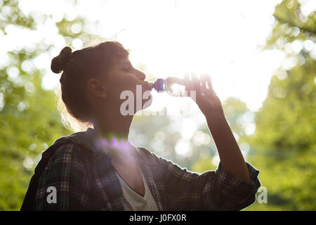 Chiusa fino ad una donna di bere acqua da una bottiglia in boschi con sushine dietro Foto Stock