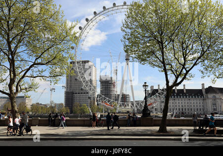 I turisti, corridori e altri pedoni passare lungo il Victoria Embankment al sole nel centro di Londra con il London Eye in background Foto Stock