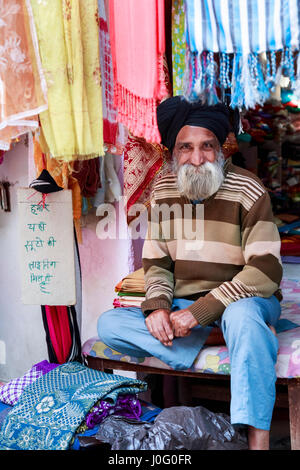 Amichevole maschio barbuto negoziante Sikh in un negozio di tessuti che indossa tipico turbante, Pragpur, un villaggio del patrimonio culturale nel quartiere Kagra, Himachal Pradesh, India Foto Stock