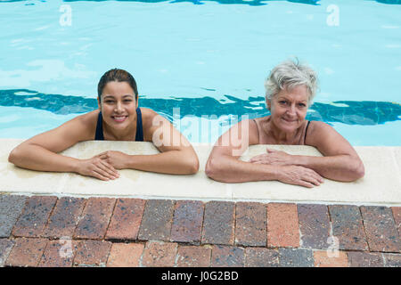 Ritratto di una donna come tuo allenatore e senior donna appoggiata sul bordo della piscina Foto Stock