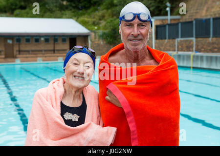 Ritratto di sorridente coppia senior avvolto in asciugamano a bordo piscina Foto Stock