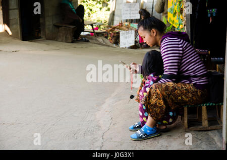 Madre di etnia Hmong figlio di parenting e la riproduzione cellulare a casa in Doi Pui villaggio tribale e parco nazionale il 28 dicembre 2016 in Chiang Mai, Thailandi Foto Stock