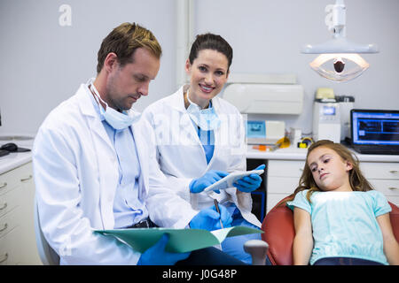 Dentisti verificando le relazioni con il paziente sdraiato sulla poltrona odontoiatrica in clinica Foto Stock