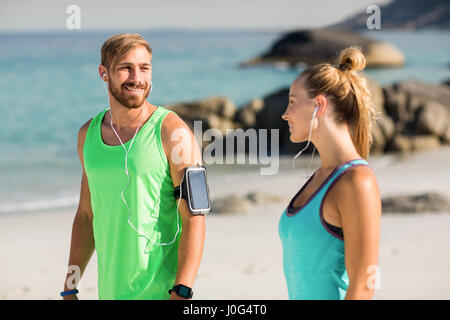 Paio di ascoltare della musica mentre si sta in piedi in spiaggia sulla giornata di sole Foto Stock