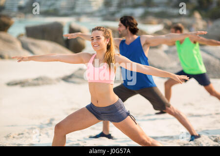 Amici praticare warrior 2 pone in riva al mare Foto Stock