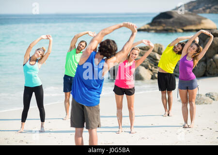 Amici in sportswear stretching mentre si sta in piedi sul litorale di spiaggia Foto Stock