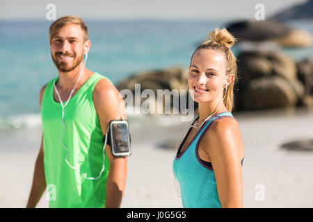 Ritratto di coppia felice in abbigliamento sportivo in piedi in spiaggia Foto Stock
