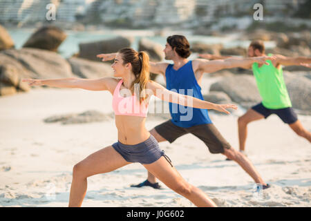 Amici praticare warrior pongono in riva al mare Foto Stock