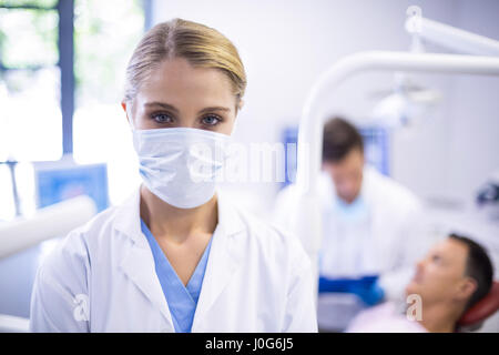 Ritratto di dentista indossando maschera chirurgica mentre il suo collega l'esame paziente in background Foto Stock