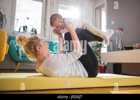 Esercizio di madre con il suo bambino sul tappeto giallo a casa Foto Stock