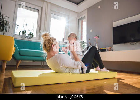 Esercizio di madre con il suo bambino sul tappeto giallo a casa Foto Stock