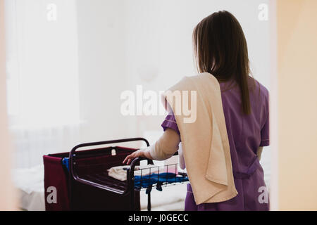 Femmina giovane cameriera spingendo il carrello durante la pulizia camere Foto Stock