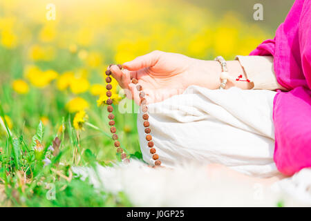 Recitazione di mantra con la mala mano durante una pratica yoga su un prato fiorito in primavera Foto Stock