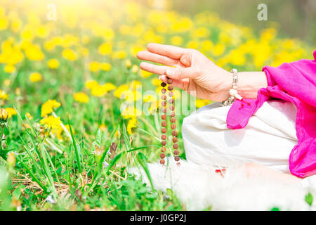 Uso di Mala con mantra durante la pratica dello yoga fiorirono nella natura Foto Stock