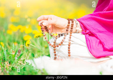 Uso di Mala con mantra durante la pratica dello yoga fiorirono nella natura Foto Stock