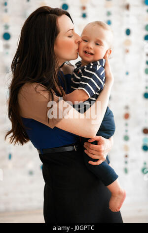 Giovane madre tiene in mano il suo bambino, abbracciando e baciando la sua. Hanno un aspetto felice. Foto Stock