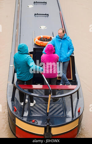 Persone su una chiatta sul canale in una piovosa giornata viaggiando lungo il Shropshire Union Canal come immettere la città mercato di middlewich cheshire, indossare abbigliamento antipioggia in quanto il pilota di barca Foto Stock