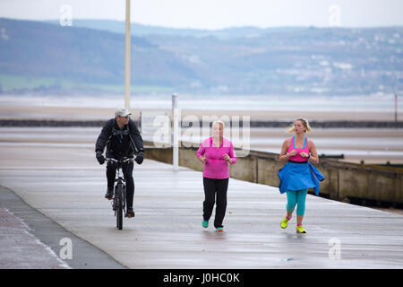 Le persone a ottenere alcuni fitness in lungo la passeggiata sul lungomare presso il famoso resort sulla spiaggia di Rhyl, Denbighshire, Galles durante bagnato estate meteo Foto Stock