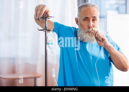 Senior uomo barbuto soffiando nel contatore di discesa in ospedale Foto Stock