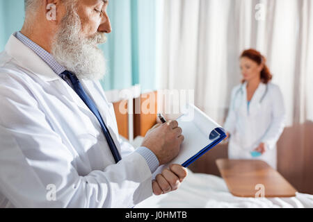 Senior medico maschio rendendo note in Appunti in ospedale Foto Stock
