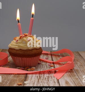 Celebrazione femminile tortina con due candele rosa, rosa caso e nastro rosa, crema di burro glassa e decorazione a stella spruzza. Sfondo semplice. Foto Stock