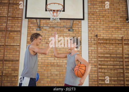 Ragazzi di liceo con basket dando un alto cinque in tribunale Foto Stock