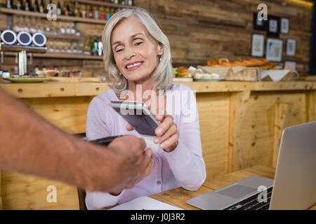 Senior donna di effettuare il pagamento tramite la tecnologia NFC sul telefono cellulare in cafÃƒÂ© Foto Stock