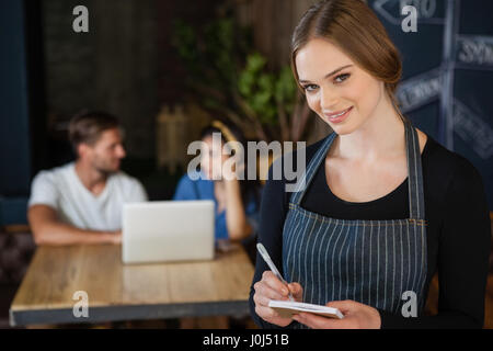 Ritratto di proprietario scrivendo su notepad mentre in piedi contro il cliente presso il cafe shop Foto Stock