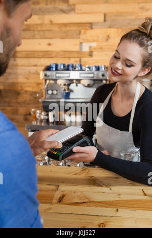 Il cliente effettuando il pagamento sul lettore di carte di credito macchina presso il cafe shop Foto Stock