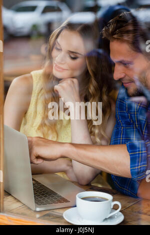 Paio utilizzando notebook digitale mentre è seduto presso il cafe shop visto attraverso il vetro della finestra Foto Stock