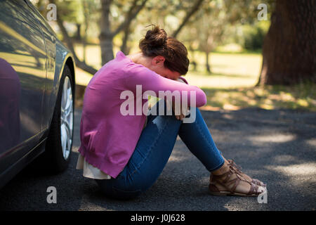Triste donna seduta dalla ripartizione auto Foto Stock