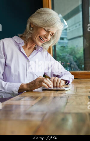 Sorridente donna senior utilizzando smart phone mentre è seduto a tavola in cafe shop Foto Stock