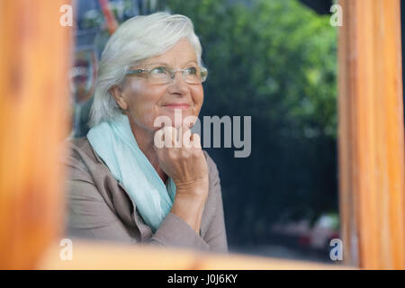 Senior donna che guarda lontano nella caffetteria negozio visto attraverso il vetro della finestra Foto Stock