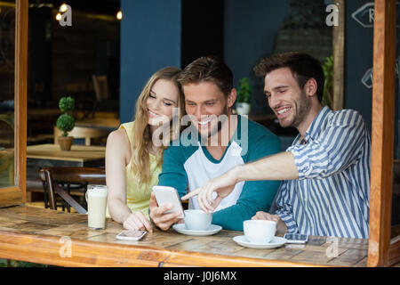 Happy amici guardando smart phone mentre seduti a tavola in cafe shop Foto Stock