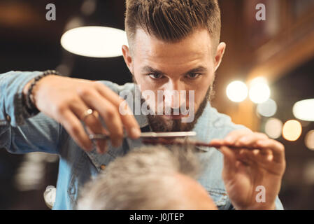 Attento giovane barbiere lavorando in Barberia Foto Stock