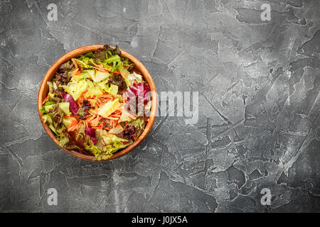 Ciotola di legno con un mix di insalata freeze, lollo rosso, radicchio, romano e iceberg con carote su sfondo grigio. Vista da sopra con posto per il testo Foto Stock
