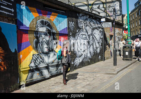 Una donna a stare di fronte ad una parete che è coperto di arte di strada a Brick Lane nella zona est di Londra. Foto Stock