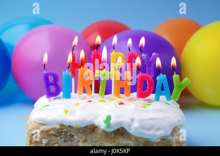 Torta con auguri di compleanno da candele accese su una di palloncini colorati sfondo Foto Stock