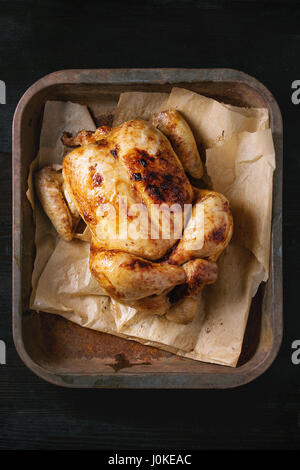 Cotta alla brace intero pollo organico sulla carta di rinforzo nel vecchio forno su nero bruciato sullo sfondo di legno. Vista superiore, vicino fino Foto Stock