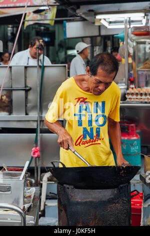 George Town, Malesia - 22 Marzo 2016: Senior uomo cuochi kway teow tagliatelle in wok Asiatici presso Kimberly cibo di strada del mercato notturno su Marzo 22, 2016 in Foto Stock