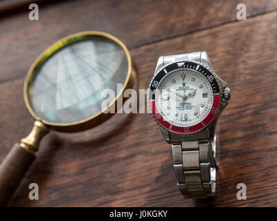 ROLEX FAKE WATCH lente di ingrandimento e fake replica contraffazione uomini orologio Rolex su una vecchia scrivania in legno top Foto Stock