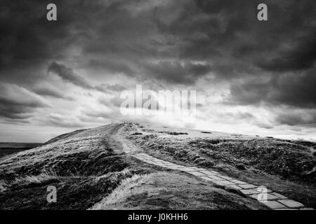 Percorso di pietra si snoda attraverso il Peak District moorland dotate di formazioni rocciose all'orizzonte e grandi meditabondo sky Foto Stock