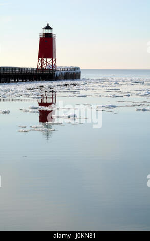 Colpo verticale di un faro rosso riflettente nel ghiaccio acqua punteggiata di lago Michigan su una tranquilla giornata invernale. Foto Stock