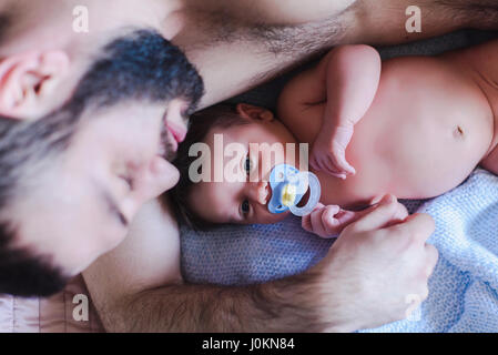 Padre Felice e un bambino. Padre e il neonato sdraiato sul letto. Il bambino con il succhietto nella bocca. Un uomo è abbracciando un bambino. Foto Stock